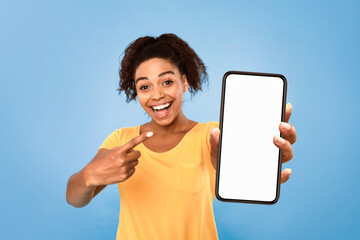 Poster - Best mobile offer, amazing online sale. Smiling African American lady demonstrating smartphone with mockup, pointing at empty screen on blue background, copy space for app or website design