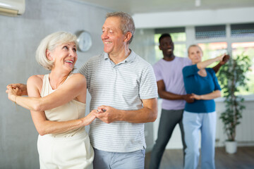 Mature male novice student of fitness studio practices paired Latin American rumba dance with elderly lady. Active hobby, movements to music, healthy lifestyle concept.