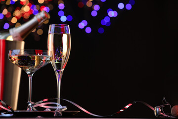 Champagne in glasses and ice bucket with bottle against black background with blurred lights, space for text