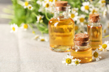 Sticker - Bottles of essential oil and chamomile flowers on cloth, closeup. Space for text