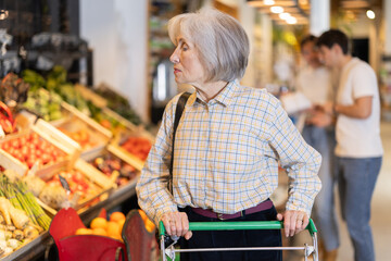 Wall Mural - Elderly woman buyer with shopping cart choosing eco products in organic grocery store