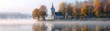 © pingpao - A serene landscape depicting a quaint church surrounded by vibrant autumn foliage and a calm lake, reflecting the tranquil beauty of nature at dawn.