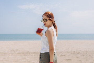 Happy woman enjoy her fresh iced tea walking on the beach.