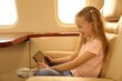 © New Africa - Cute little girl using tablet in airplane during flight
