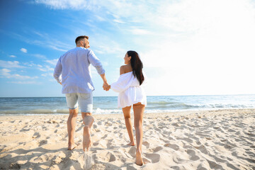 Wall Mural - Happy couple running together on beach, back view