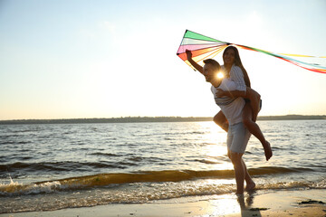 Wall Mural - Happy couple playing with kite on beach near sea at sunset. Spending time in nature