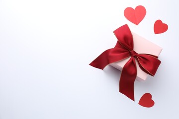 Wall Mural - Gift box with red bow and paper hearts on white background, flat lay. Space for text