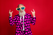 © deagreez - Photo of funky aged man amour cupid character role showing horns fingers excited emotions wear sun specs hearts pattern suit costume shirt tie isolated red color background