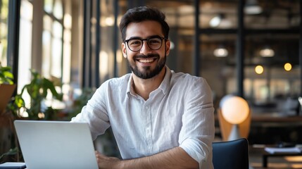 Aufkleber - In a spacious, vibrant office filled with natural light, a cheerful man works diligently on his laptop. His friendly smile reflects dedication while surrounded by greenery and contemporary decor