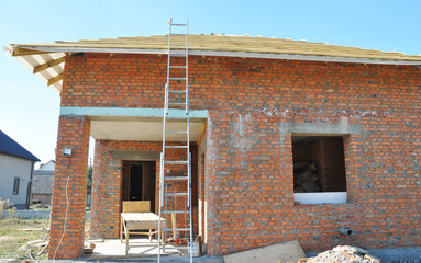 Wall Mural - An aluminum extension ladder is attached to a house being built of brick during roofing construction.