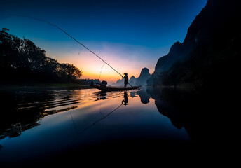 Poster - China landscape view depicting a person fishing from a boat on a calm river at dusk. Mountains and a colorful sky complete the tranquil scene.
