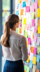 Poster - Woman Analyzing Colorful Sticky Notes on Wall in Modern Office Space, Engaged in Creative Planning