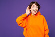 © ViDi Studio - Young smiling curious nosy happy Caucasian woman she wear orange hoody casual clothes try to hear you overhear listen intently isolated on plain purple background studio portrait. Lifestyle concept
