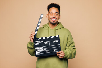 Poster - Young man of African American ethnicity wear green hoodie casual clothes hold in hand classic black film making clapperboard isolated on plain pastel light beige background studio. Lifestyle concept.