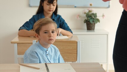 Poster - bored elementary student looking at teacher while attend in classroom. diverse smart student sitting