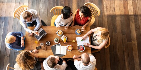 Poster - Top view of a diverse group of people having a meeting around a wooden table with laptops and documents. Collaborative team discussion in a office. Casual startup business team working at a cafe.