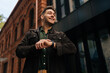 © dikushin - Cheerful handsome young man using smartwatch to check time, read notifications and navigate apps while standing in urban outdoor setting. Concept of modern successful city lifestyle.