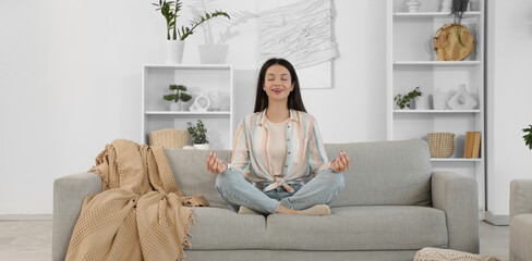 Wall Mural - Beautiful young woman meditating on cozy sofa at home