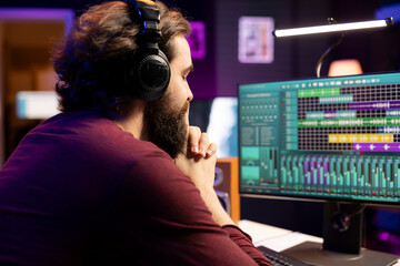 Leinwandbilder - Music engineer listening his audio recording on headset after editing and adding new sound effects in home studio. Producer using daw software interface on pc to enhance music volume, stereo tool.