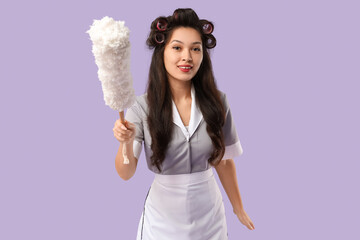 Poster - Young Asian chambermaid with hair curlers and pp-duster on lilac background