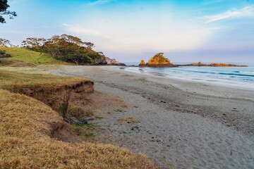 Wall Mural - Tranquil beach scene at dawn. Gentle waves lap the shore, rocky outcrop in the distance. Peaceful coastal landscape. Elliot Bay, Rawhiti, Northland, New Zealand