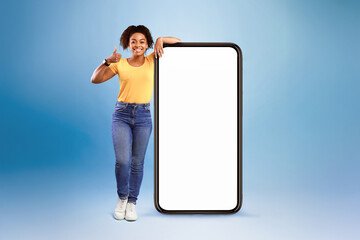 Poster - Mobile offer. Happy African American lady leaning on huge cellphone with empty white screen, showing thumb up, recommending cool new app or website, offering space for your ad, mockup