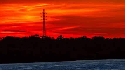 Wall Mural - orange, red sunset over forest and river. silhouette of a high voltage pole against the sunset. sky 