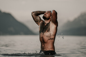 Wall Mural - Sexy summer man. Muscular body. Hot summer. Man swimming in lake. Nude male body. Guy splash in water in summer nature. Fit male model posing by summer beach. Strong man splashing in a mountain lake.