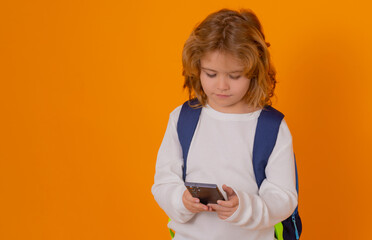 Fototapete - Smart child, clever school kid. School child with backpack using phone isolated on yellow color background.