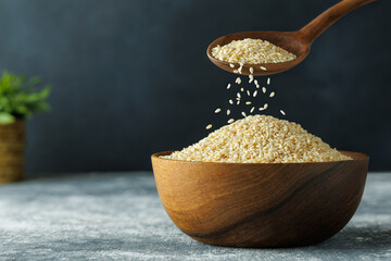 Wall Mural - sesame seeds falling from spoon in bowl on table