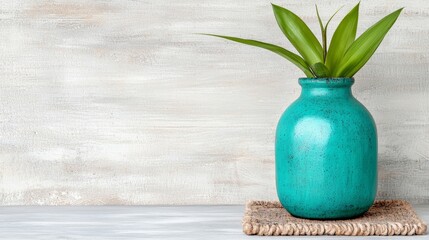 Wall Mural -  a blue vase with a plant in it sitting on top of a table, with a mat beneath it and a wall in the background