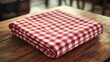 © Oleg - A red and white checkered towel folded neatly on a wooden dining table.