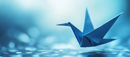 Leinwandbilder - Blue origami paper crane elegantly positioned in the foreground against a soft blue gradient background with shimmering bokeh effects.