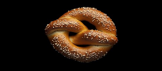 Poster - Aerial view of a soft pretzel sprinkled with sesame seeds against a contrasting dark background, showcasing its golden brown texture and twisted shape.