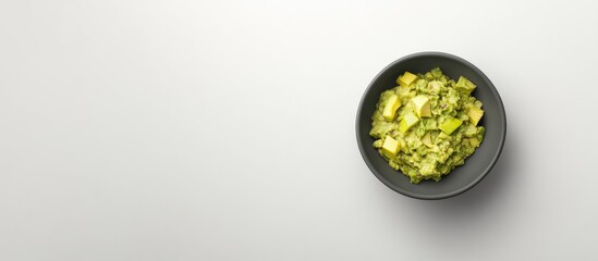 Poster - Guacamole in a black bowl with chunks of avocado on a light grey background, top view showcasing vibrant green colors and texture contrast.