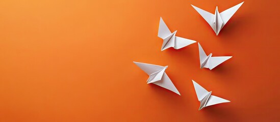 Poster - White origami birds arranged on a vibrant orange background showcasing a clean flat lay design with dynamic shapes and shadows on the surface