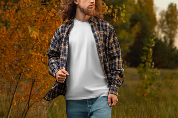 Wall Mural - White T-shirt mockup on a guy walking against a nature background in a plaid flannel shirt.