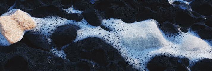 Poster - Textures of black sand with pumice stones along the shoreline at low tide