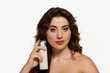 © LIGHTFIELD STUDIOS - Stylish young woman showcasing a beauty product with confidence and charm in a bright setting