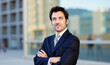© Minerva Studio - Portrait of a businessman smiling with arms crossed in front of modern buildings