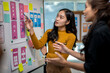 © Wasana - Two women are looking at a white board with a lot of sticky notes on it
