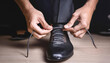 © lina - person carefully tying the laces of an elegant black dress shoe.