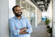 © antusher - Smiling Indian man with a beard standing in a bright modern office hallway