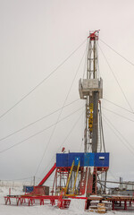 Wall Mural - Industrial winter landscape featuring an operational drilling rig with support facilities at a remote worksite during daylight hours