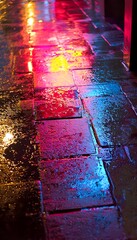 Poster - Close-up of a rain-drenched urban alley, glowing neon signs reflecting dynamic textures on wet surfaces, cinematic storytelling