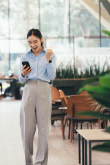 Poster - Enthusiastic Asian professional celebrating business success, raising fist triumphantly while checking smartphone in contemporary workplace, displaying vibrant career momentum