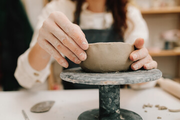 Poster - Craftswoman carefully molds a clay bowl on the potters wheel. Creating ceramic crockery in the workshop.