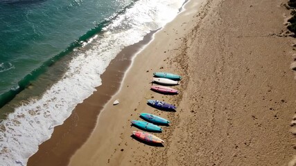 Aufkleber - Gentle ocean waves roll onto a sandy beach where colorful surfboards lie in the sand, creating a calming and picturesque scene in slow motion