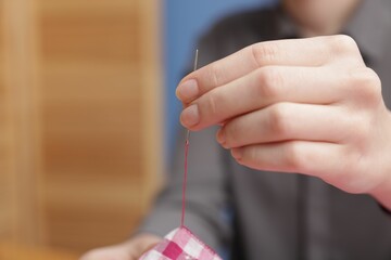 Wall Mural - Woman sewing cloth with thread on blurred background, closeup. Space for text