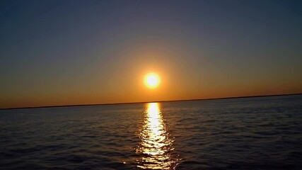 Wall Mural - slow motion shot of a breathtaking sunset over vast water – radiant sun near the horizon, golden hue